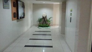 A hallway with a tiled floor, a reception desk, and a plant arrangement. - Sewaunitkalcit (Jakarta)