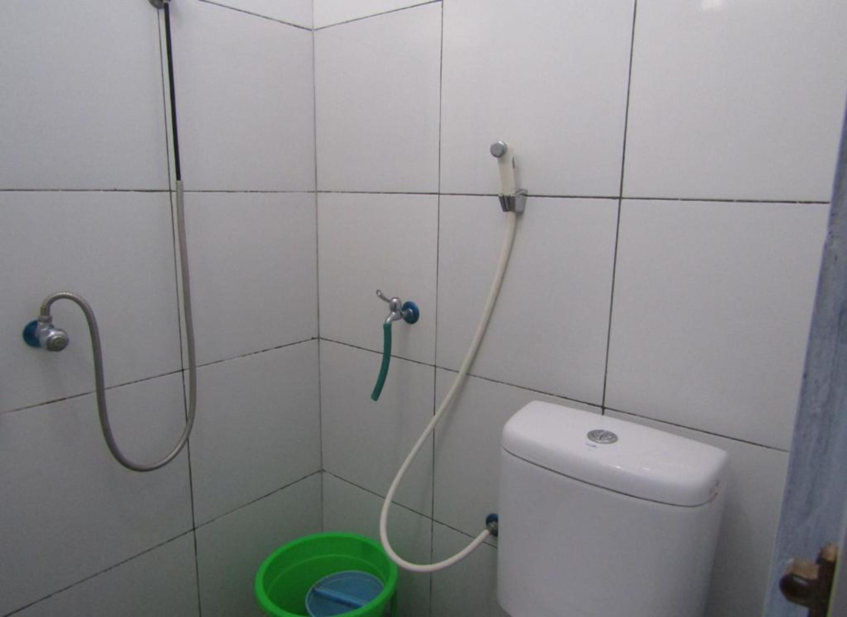 A small, tiled bathroom with a toilet, a green bucket, and two showerheads.