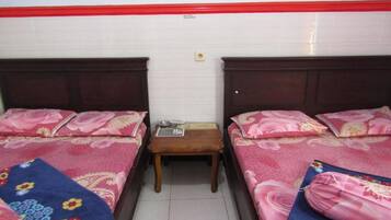 A room with two single beds, each with a floral bedspread and matching pillows. There is a small wooden nightstand between the beds with a few items on it. The room has white walls and a red trim at the top.