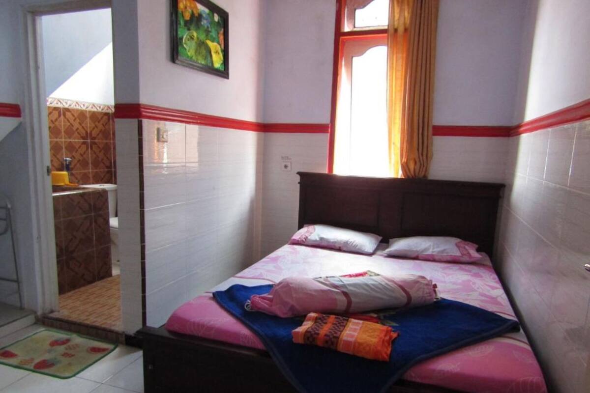 A bedroom with a bed, a window with curtains, and a bathroom visible through an open door.