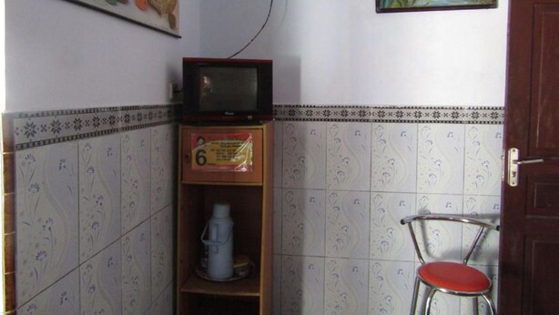 Una habitación pequeña con una televisión sobre una estantería de madera, una silla con asiento rojo y dos cuadros en la pared.