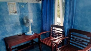 A room with blue tiled walls, a wooden table with a fan, and two wooden chairs. - Hotel Abimanyu Bandungan (Bandungan)