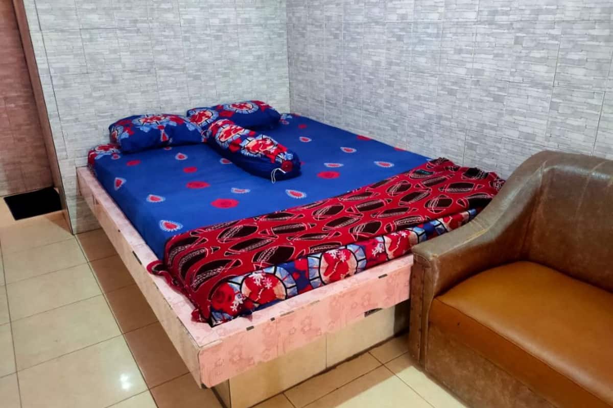 Une petite pièce carrelée, avec un lit recouvert d’une couette à motifs et un canapé en cuir marron.