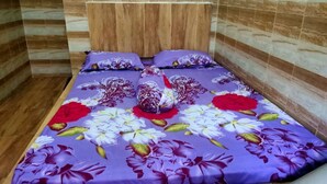 A bed with a floral bedspread and matching pillows in a room with wooden paneling and tiled walls. - Hotel Abimanyu Bandungan (Bandungan)