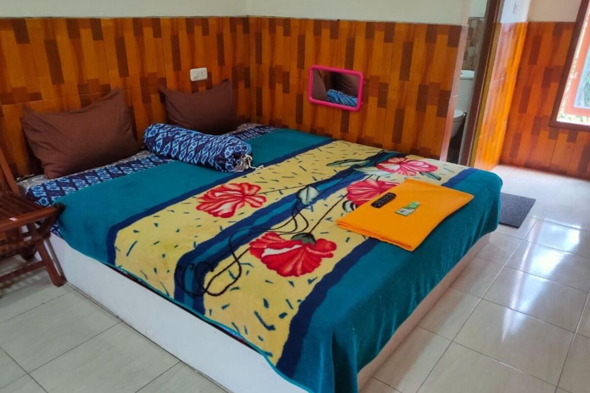 A bed with a floral bedspread, a small mirror, and a folded orange item on the bed.