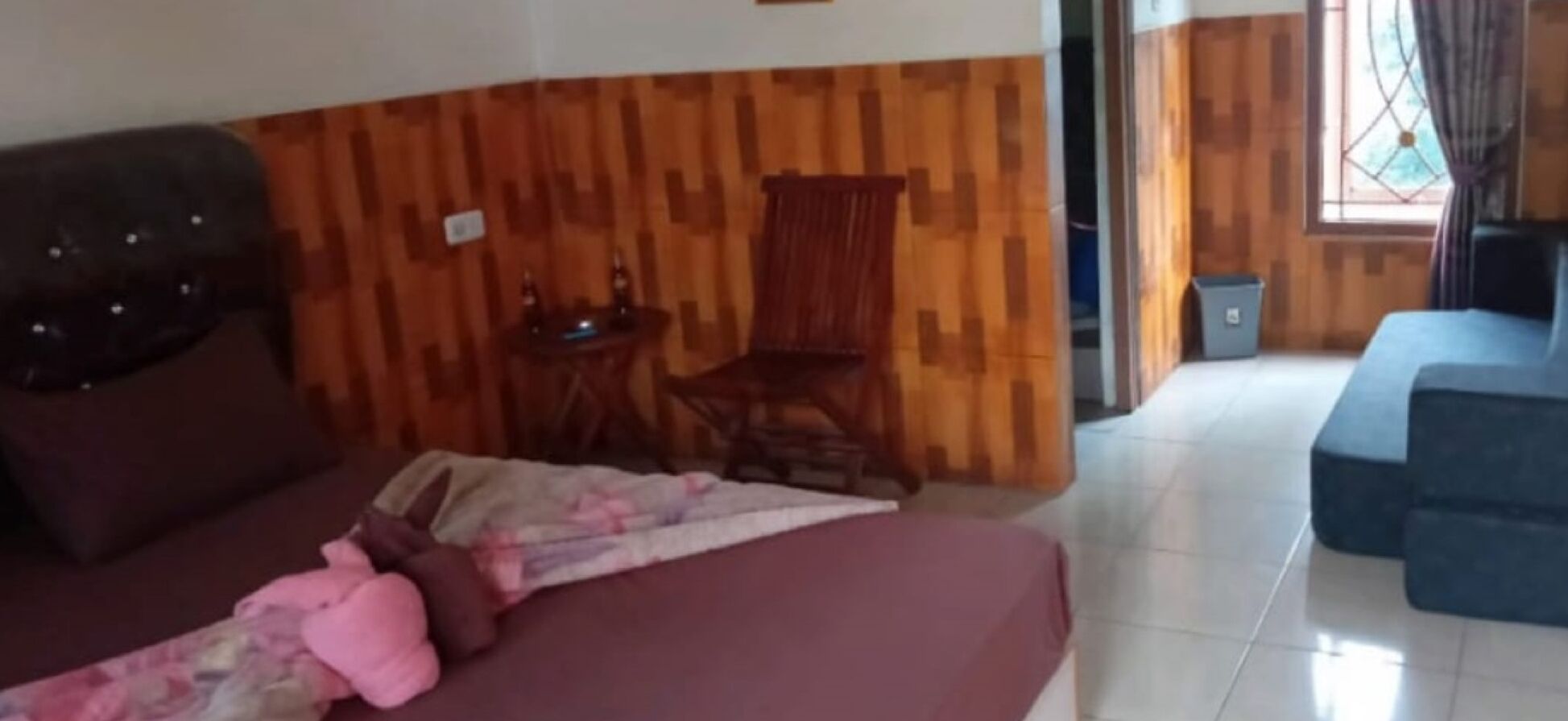 A room with a wooden wall, a bed with a pink blanket, a wooden chair, and a blue sofa.