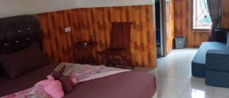 A room with a wooden wall, a bed with a pink blanket, a wooden chair, and a blue sofa.