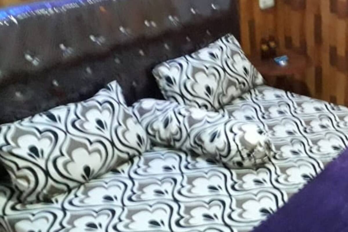 Ein Zimmer mit Schlafsofa, dessen Bezug ein schwarz-weißes Muster aufweist, einem Holzkopfteil und einem kleinen Tisch mit einer Dekoration.