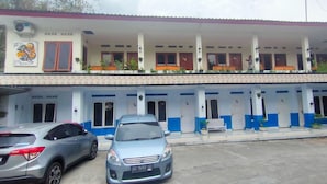 Ein Hotel mit zweistöckiger Bauweise, mehreren Zimmern mit blauen und weißen Wänden sowie einem überdachten Außenbereich mit Bänken und Topfpflanzen.