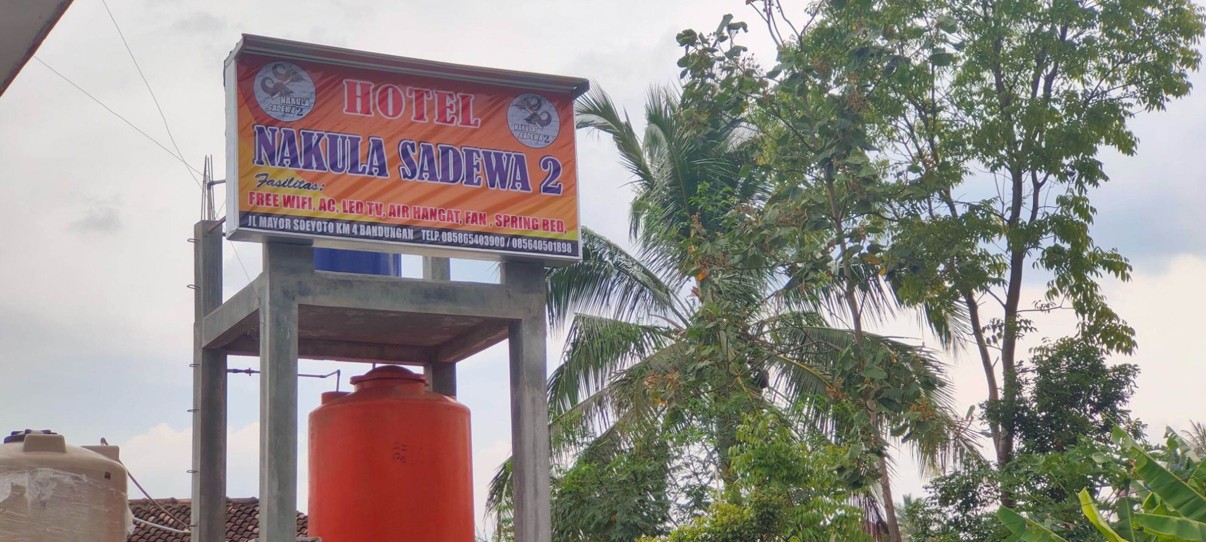 A hotel signboard with amenities listed, including free WiFi, AC, LED TV, air conditioning, fan, and spring beds.