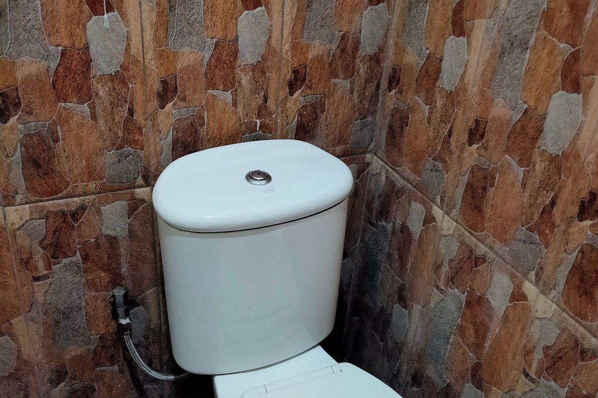 Eine Toilette mit weißem Tank und Sitz, vor einer Wand mit Mosaikfliesen in Braun- und Grautönen.