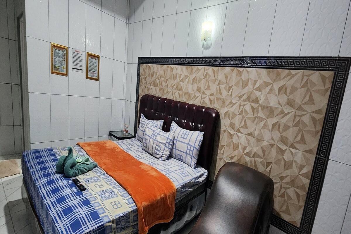 Ein Schlafzimmer mit einem Bett, einem Sessel und einer gefliesten Wand mit geometrischen Mustern.