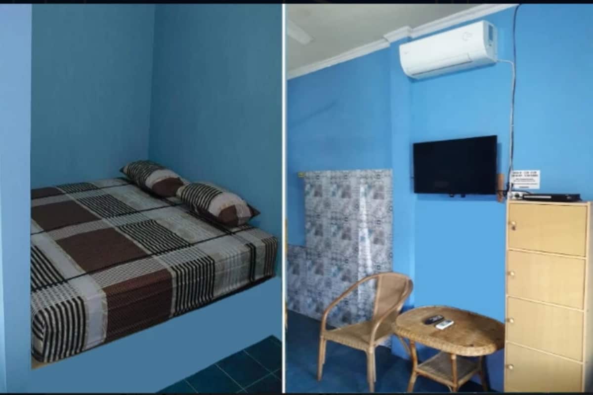 A room with a bed, a chair, a small table, a television, and a wardrobe.