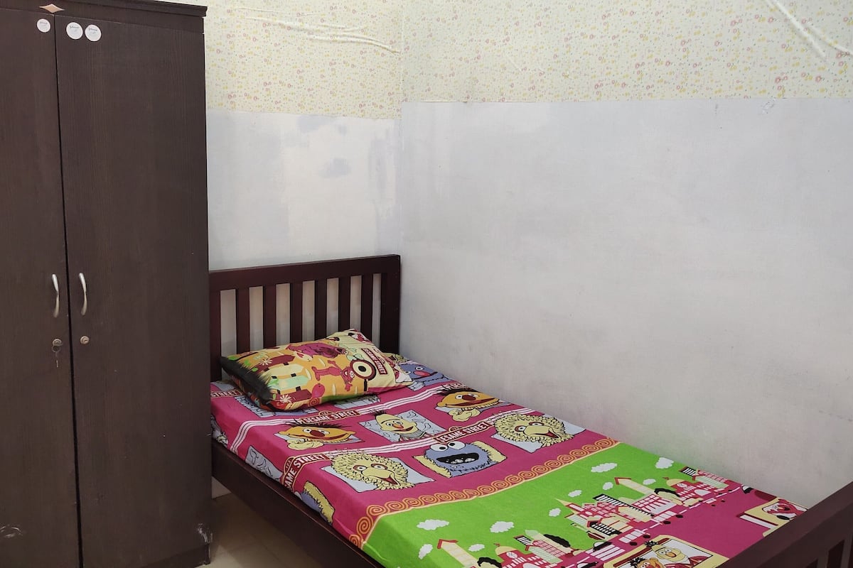 A small bedroom with a single bed, a wooden wardrobe, and a floral-patterned wall.