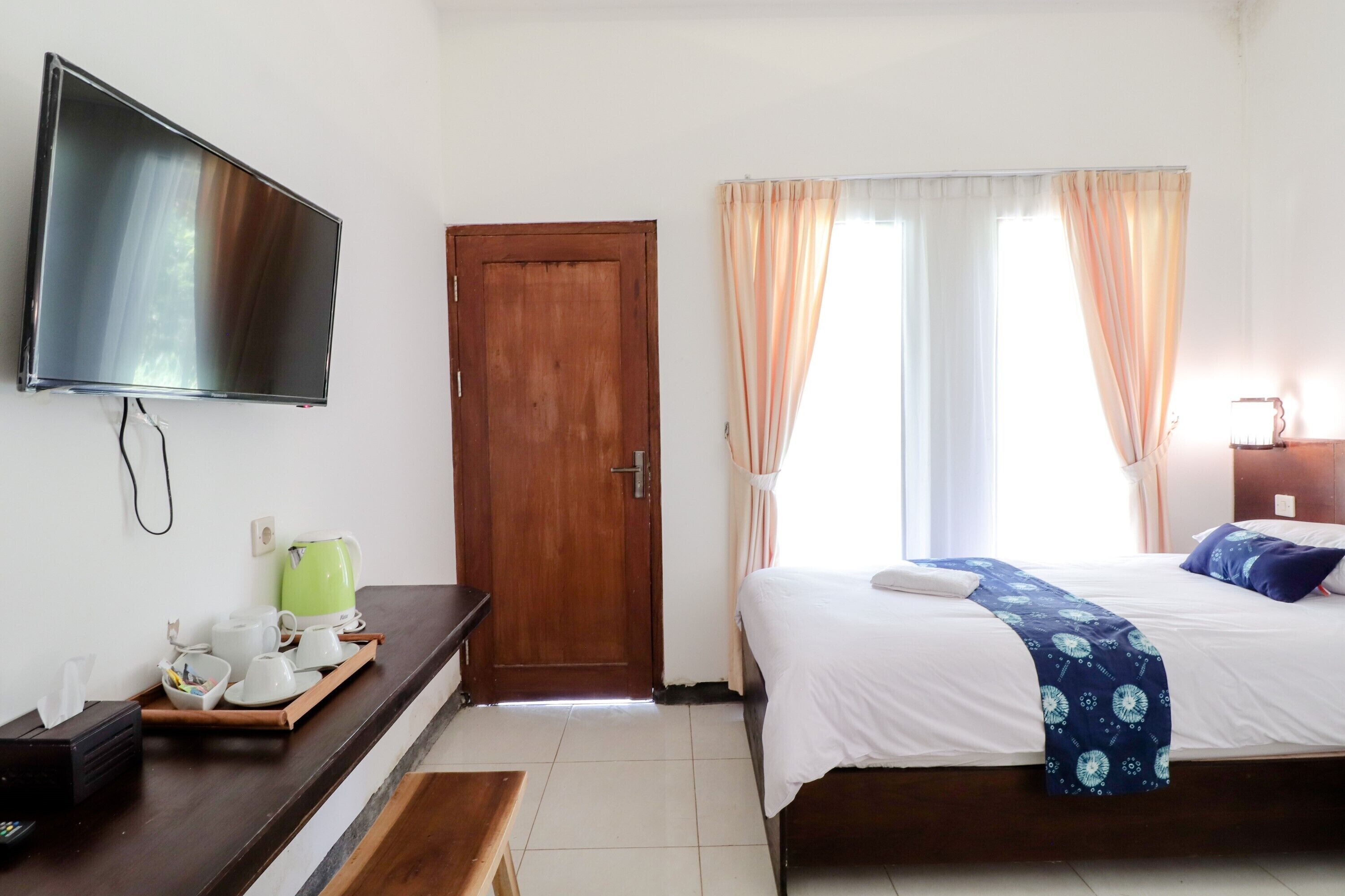 Een hotelkamer met een bed, een aan de muur bevestigde televisie, een houten deur en een raam met gordijnen.