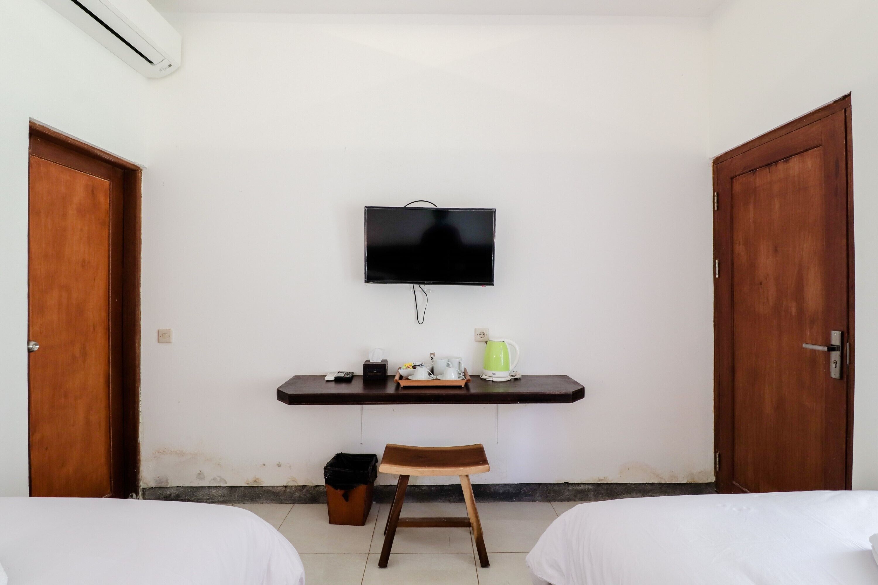 Une chambre avec deux lits, un téléviseur fixé au mur, une petite table avec une bouilloire et des tasses, et une poubelle.