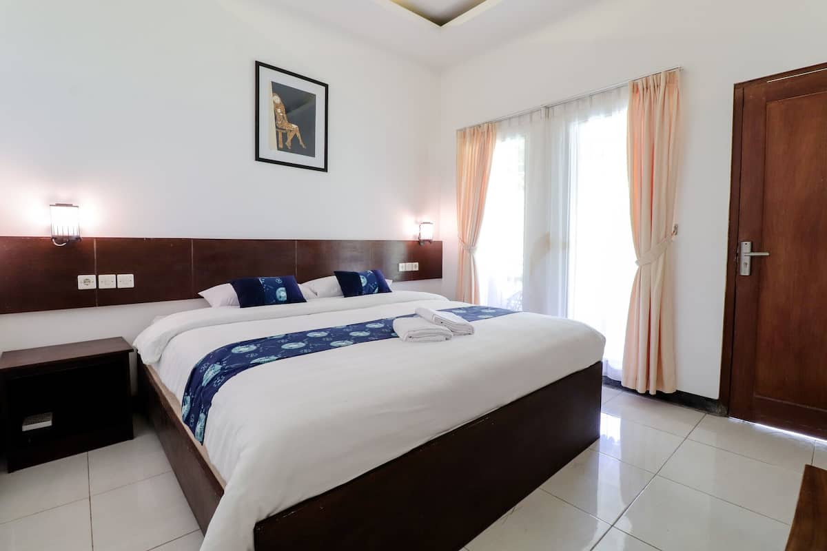 Una habitación de hotel con una cama grande, lámparas de noche, un cabecero de madera, un cuadro en la pared y una puerta.