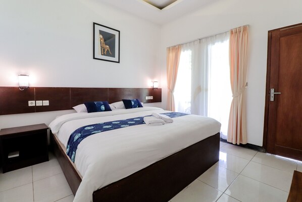 A hotel room with a large bed, two bedside tables, a nightstand, a framed picture on the wall, and a door. - Balkondes Kenalan (Borobudur)