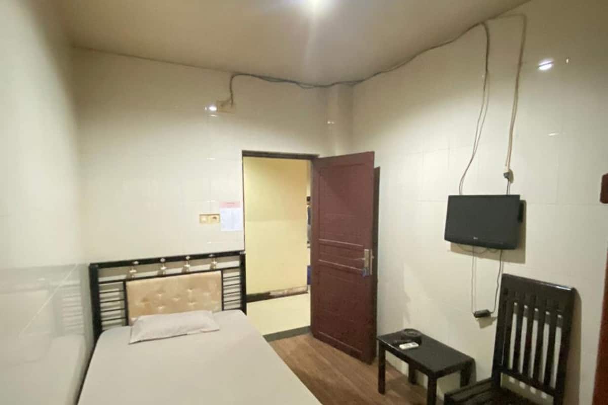 A bedroom with a bed, a TV mounted on the wall, a chair, and a small table.