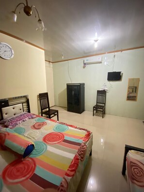 A bedroom with a bed, two chairs, a wardrobe, a television, and a clock on the wall.