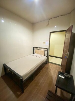 A small, single-bed room with a wooden floor, a bedside table, and a mirror on the wall.