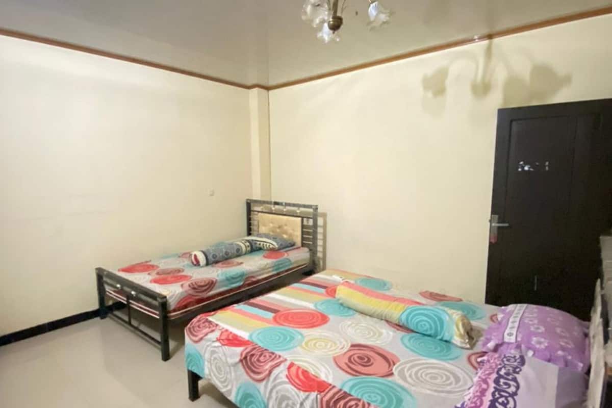 A room with two beds, a ceiling light fixture, and a door.
