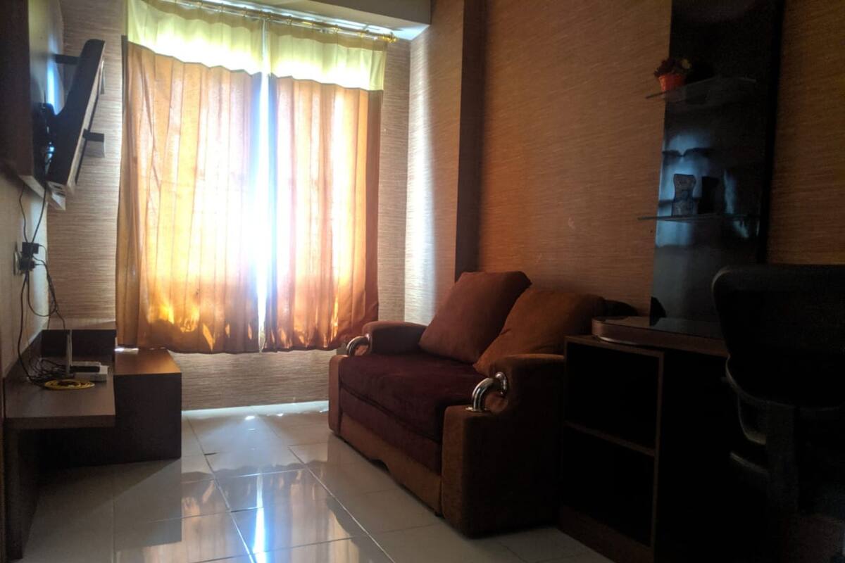 A living room with a sofa, a TV, a coffee table, and a window with curtains.