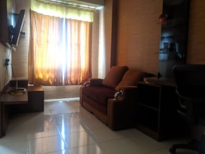 A living room with a sofa, a TV, a coffee table, and a window with curtains. - Pinewood Apartment by Vial (Cileunyi)