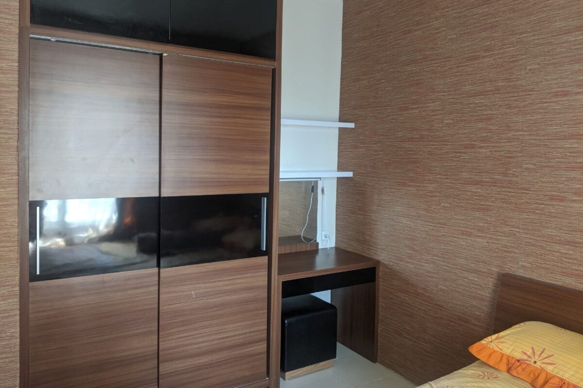 A bedroom with a wooden wardrobe, a desk, and a bed with a pillow.