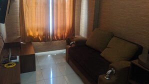 Una sala de estar con un sofá marrón oscuro, una mesita auxiliar y un televisor sobre un mueble de madera.