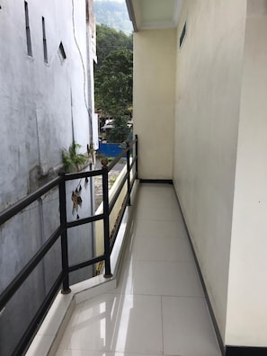 A narrow corridor with tiled flooring, a black metal railing, and a view of a blue pool and greenery in the background. - Villa Bintang (Malang)