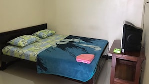 A single bed with floral bedding, a blue blanket, and a pink towel. A television is on a wooden stand beside the bed. - Villa Bintang (Malang)