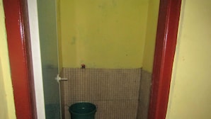 A small, narrow bathroom with a toilet, a green bucket, and a red door frame. - Hotel Kopeng Indah 1 (Getasan)