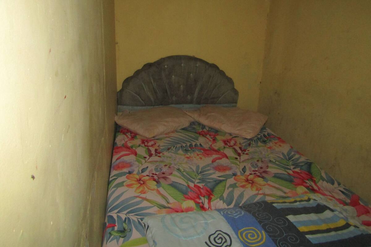 A small, narrow room with a single bed featuring a floral bedspread and a headboard.