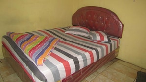 A single bed with a striped bedspread and pillows, a red headboard, and a yellow wall. - Hotel Kopeng Indah 1 (Getasan)