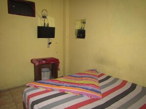 A small, sparsely furnished room with a bed, a television mounted on the wall, and a small table with a basket. - Hotel Kopeng Indah 1 (Getasan)
