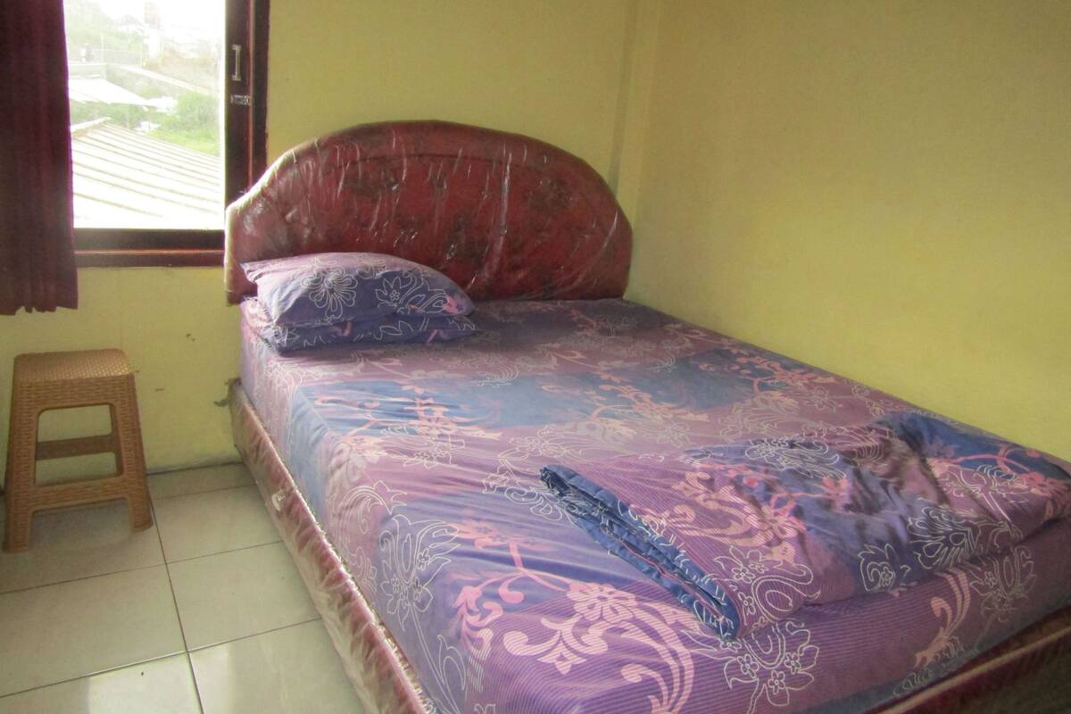 A small, single-bed room with a wooden headboard and a window with curtains.