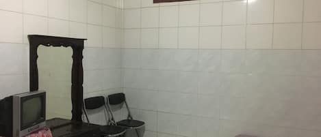 A small, tiled room with a television, a mirror, two chairs, and a bed with a floral bedspread.