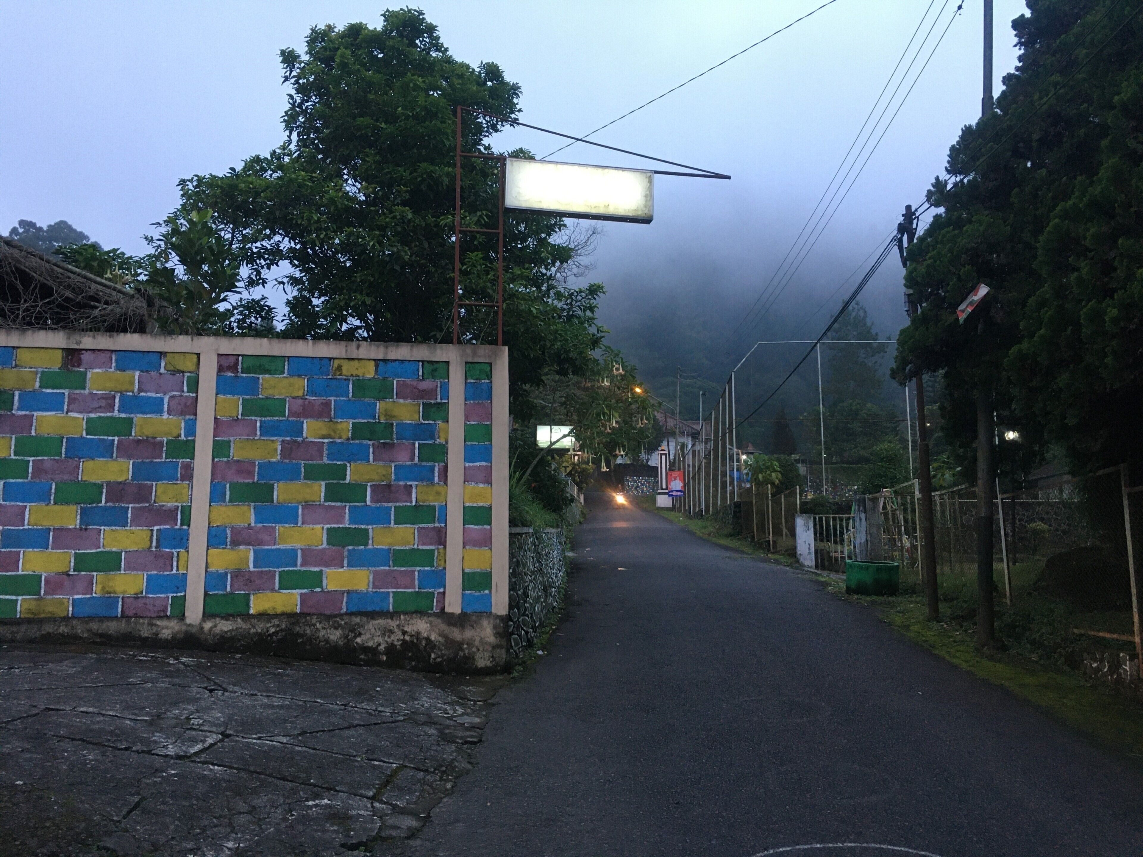 A narrow road with a colorful brick wall on the left.