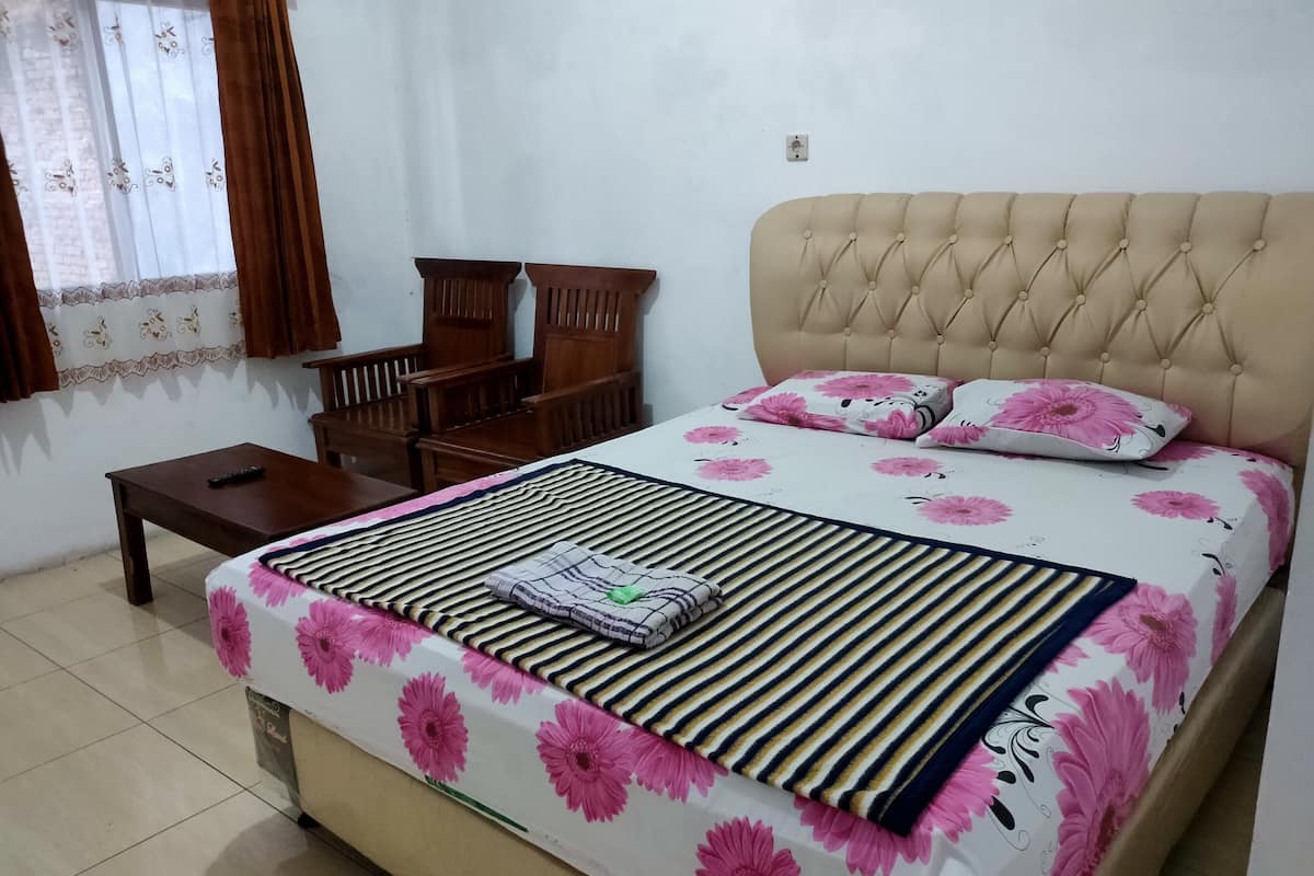 Un dormitorio ordenado con cama, mesita de noche, silla y ventana con cortinas.