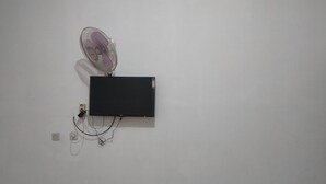 Een zwarte flatscreen televisie bevestigd aan een witte muur, aangesloten op een stekkerdoos met twee stopcontacten.