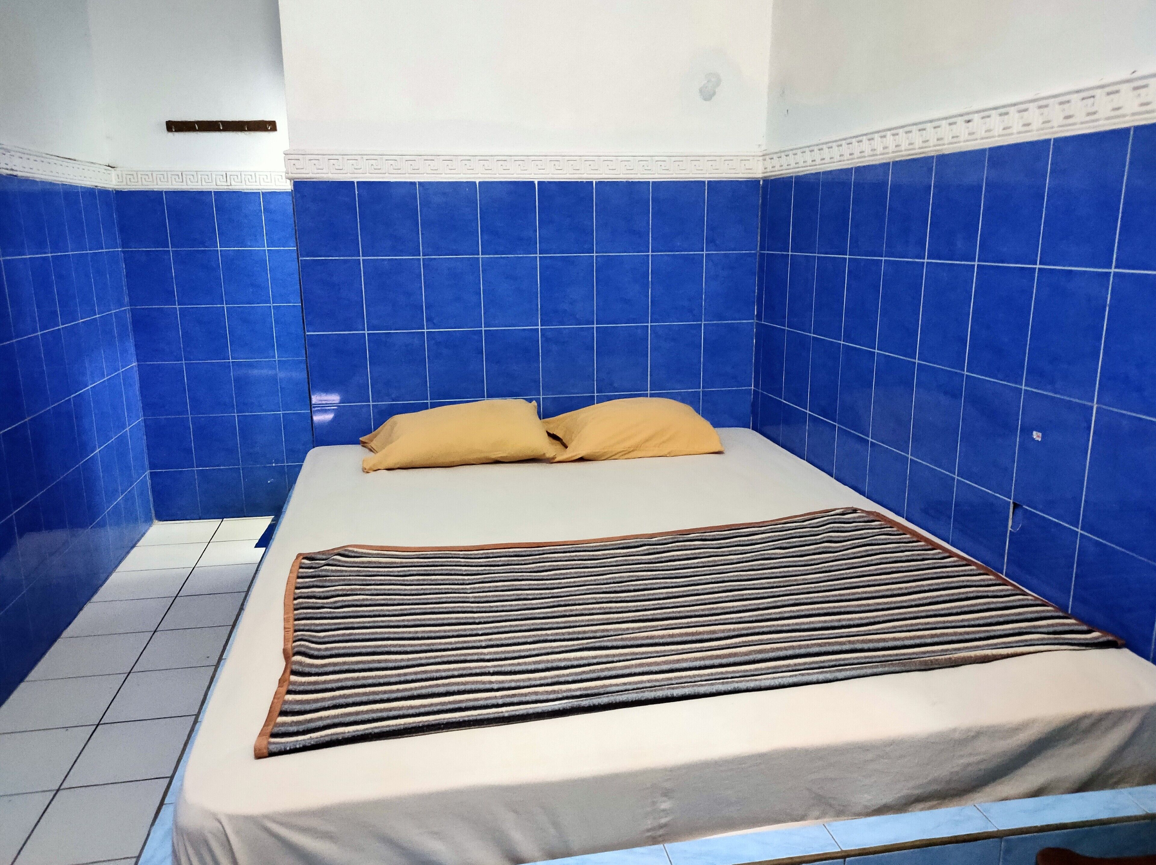 A small, single-bed room with blue tiled walls and a white floor.