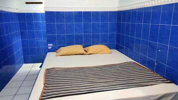 A small, single-bed room with blue tiled walls and a white floor.