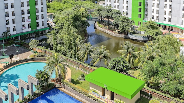 A high-rise hotel with a swimming pool, lush greenery, and a small building with a green roof. - Juragan Room (South Tangerang)