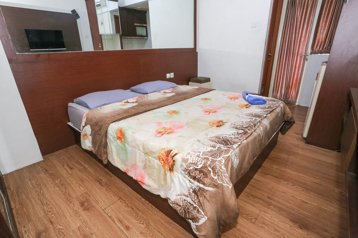 A bedroom with a wooden floor, a bed with a floral bedspread, a nightstand, and a mirror above the bed.