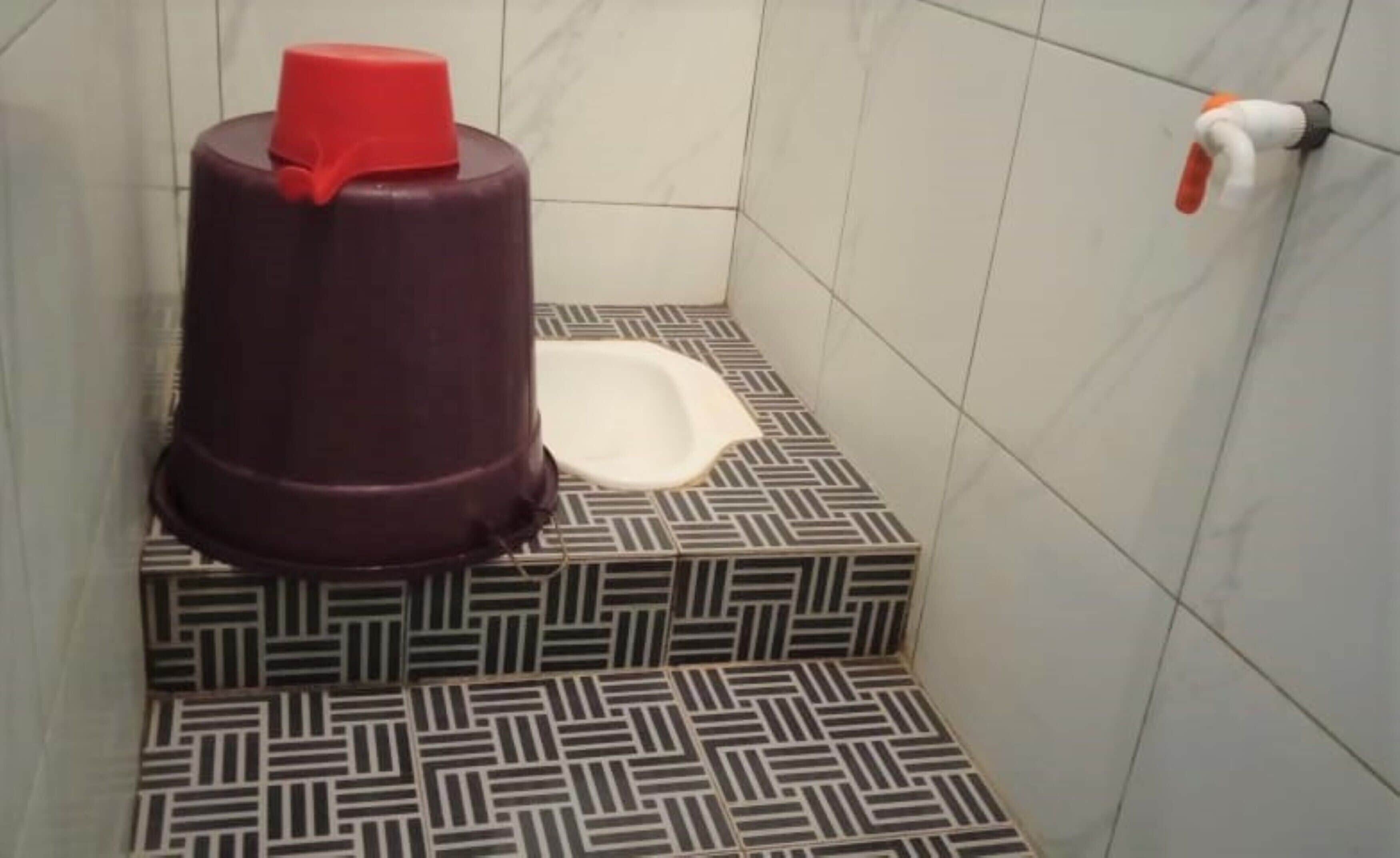 Un baño con piso estampado, un inodoro blanco y un recipiente rojo.