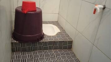 Un baño con piso estampado, un inodoro blanco y un recipiente rojo.
