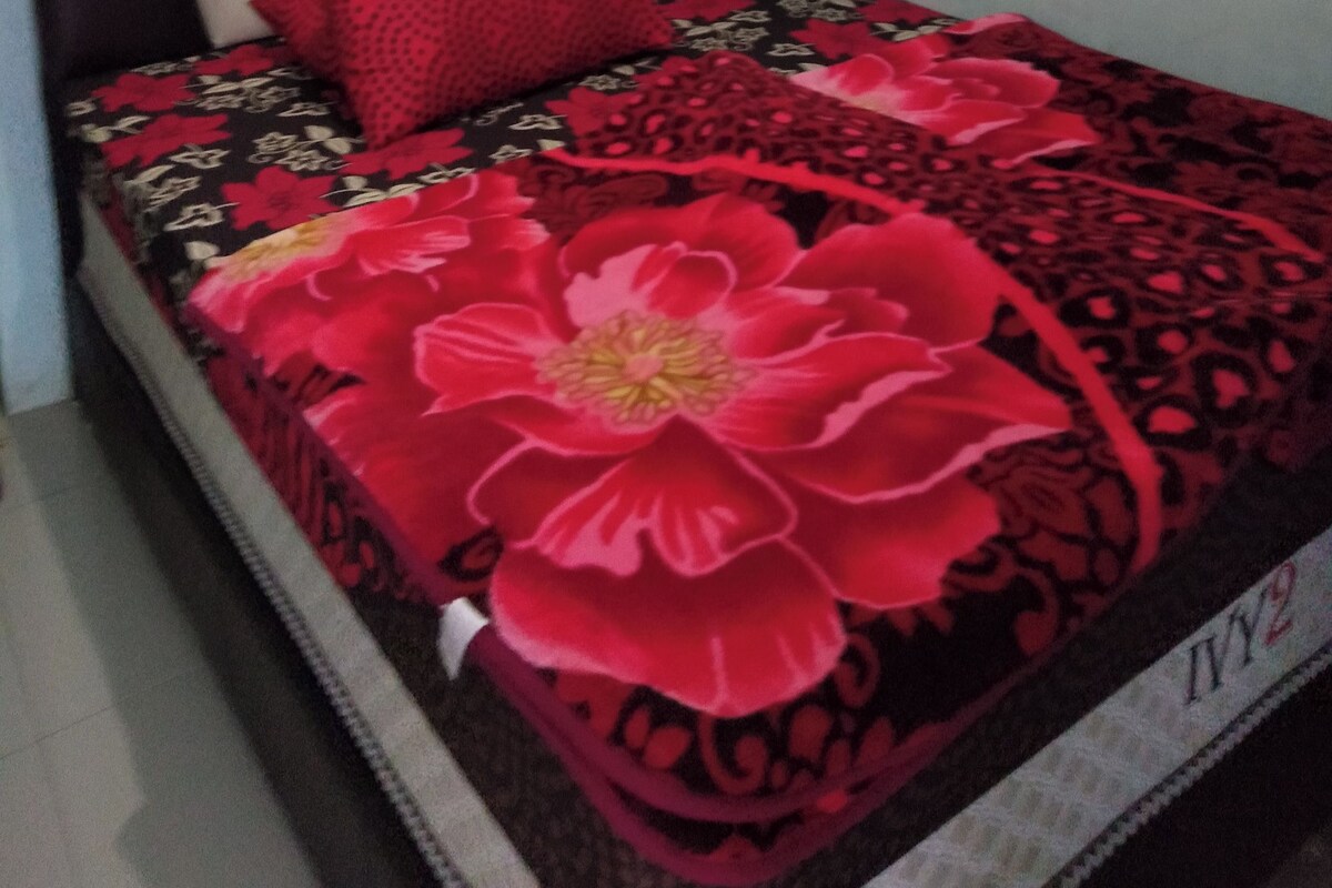 A bed with a floral bedspread, a red pillow, and a headboard.