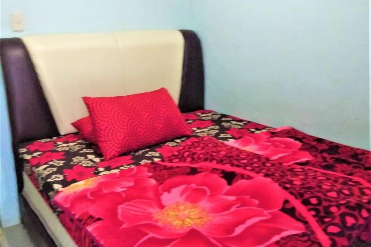 A single bed with a headboard, a red pillow, and a floral bedspread.
