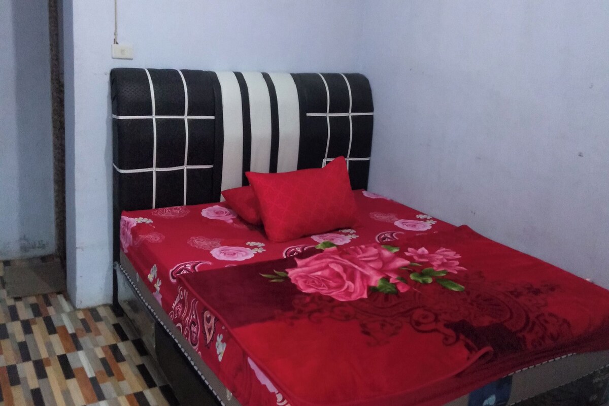 A room with a bed featuring a black and white headboard, a red floral bedspread, and a patterned floor.